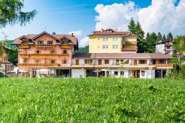 Kolorowy hotel wielopiętrowy, otoczony zielenią i niebieskim niebem.