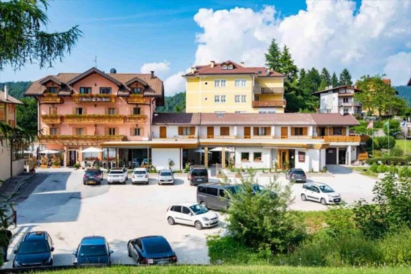Hotel z oświetloną fasadą i parkingiem pełnym samochodów o zmierzchu.
