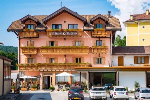 Hotel oświetlony o zmierzchu z kilkoma zaparkowanymi przed nim samochodami.