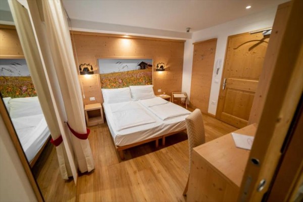 Nowoczesny pokój hotelowy z drewnianymi meblami i obrazem górskiej łąki nad łóżkiem.