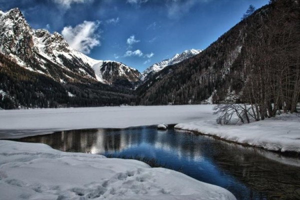 Zamarznięte jezioro otoczone ośnieżonymi górami pod niebieskim niebem.
