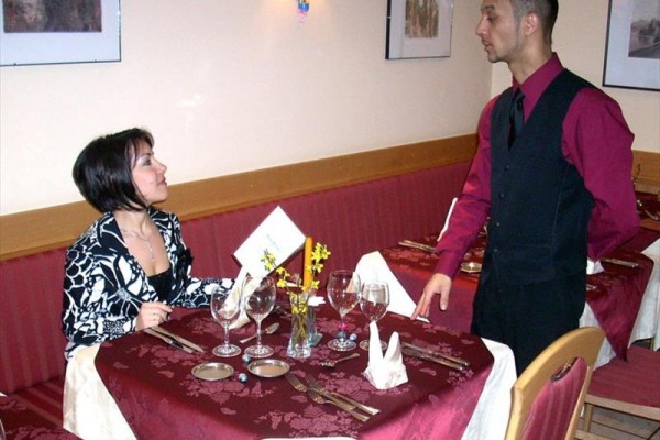 Kobieta siedząca przy stole w restauracji rozmawia z kelnerem stojącym obok.