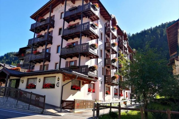 Wielopiętrowy hotel z drewnianymi balkonami i kwiatami w malowniczej górskiej okolicy.
