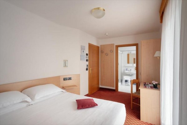 Pokój hotelowy z łóżkiem małżeńskim i wejściem do łazienki.