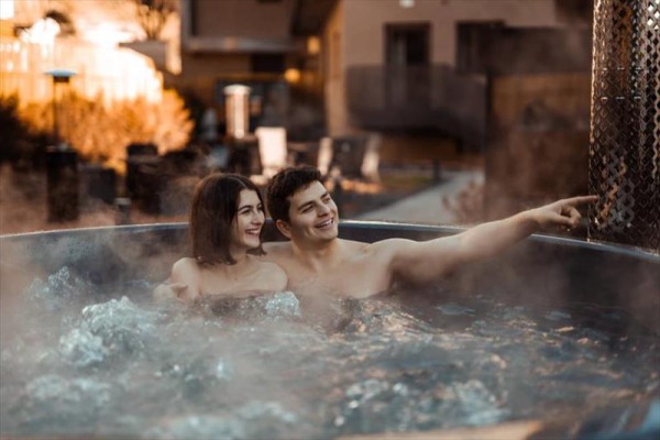 Dwie osoby uśmiechają się i relaksują w zewnętrznej wannie z hydromasażem otoczonej parą.