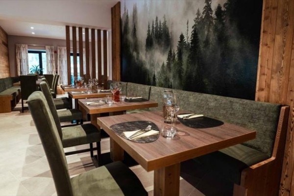 Restauracja z drewnianymi meblami i malowidłem lasu na ścianie.