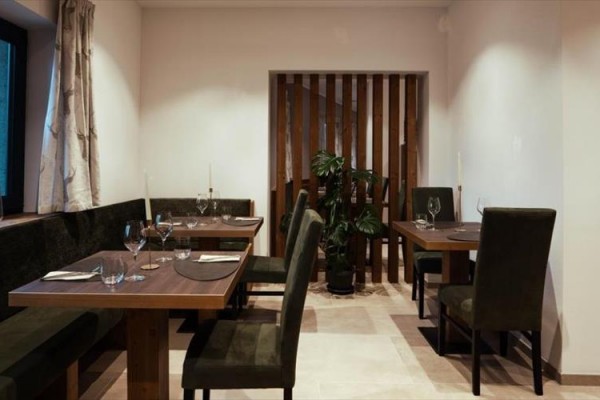 Restauracja z drewnianymi stołami, prostymi meblami i rośliną w rogu.