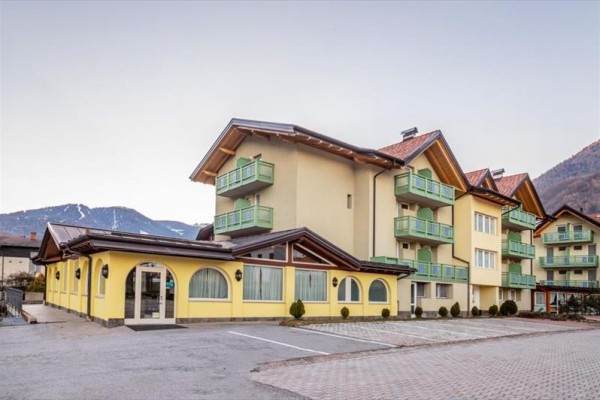 Żółty budynek hotelu z balkonami w górskiej okolicy.