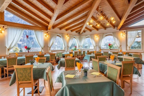 Jasna restauracja z drewnianym sufitem, zielonymi obrusami i dużymi oknami z widokiem na góry.