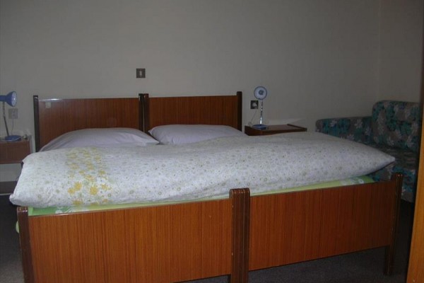 Drewniane łóżko z dwoma lampkami na stolikach nocnych i kwiecistą kanapą w tle.