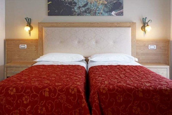 Dwa pojedyncze łóżka z czerwonymi narzutami w hotelowym pokoju ze ściennymi lampami.