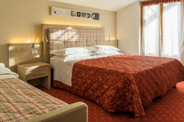 Pokój hotelowy z dużym łóżkiem, tapicerowanym zagłówkiem i dekoracyjnym obrazem na ścianie.