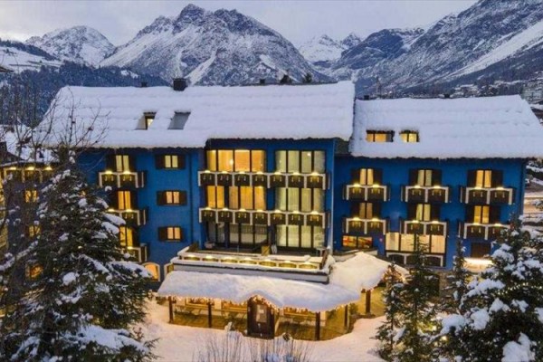 Niebieski budynek hotelu pokryty śniegiem w zaśnieżonych górach.