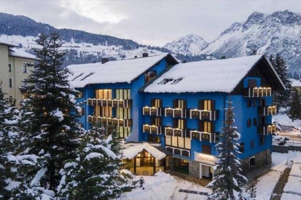 Niebieski hotel otoczony ośnieżonymi górami i drzewami.