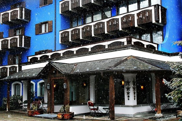 Niebieski hotel z drewnianymi balkonami podczas opadów śniegu.