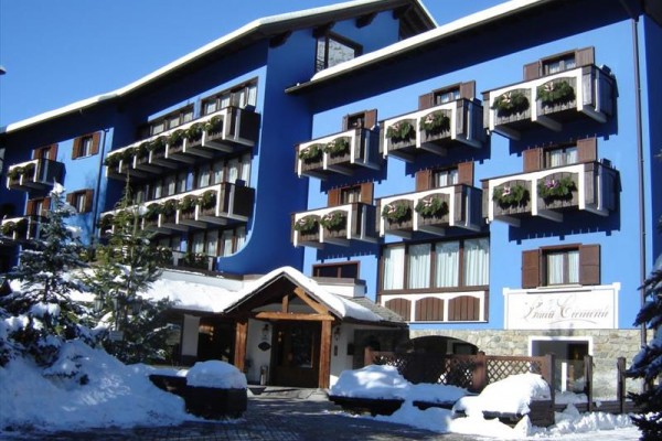 Niebieski hotel z drewnianymi balkonami ozdobionymi kwiatami w ośnieżonym otoczeniu.