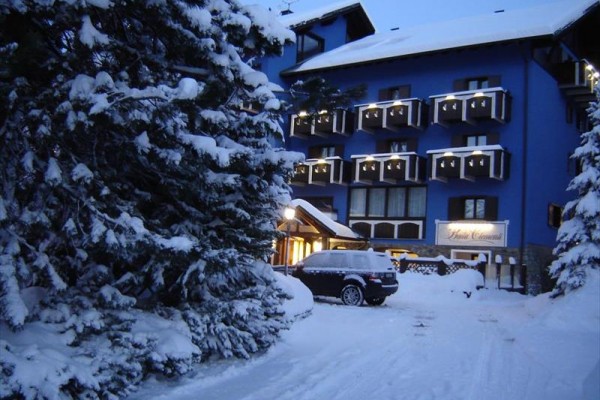 Zaśnieżony hotel z niebieską fasadą i balkonami w wieczornym oświetleniu.