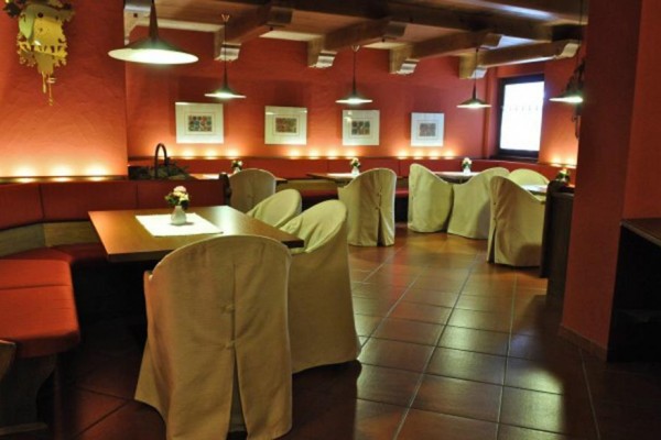 Restauracja z drewnianymi stołami, czerwonymi ścianami i krzesłami z białymi pokrowcami.