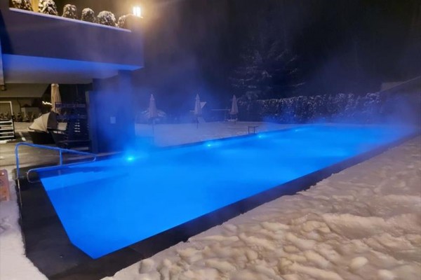 Ogrzewany basen zewnętrzny z niebieskim oświetleniem otoczony śniegiem nocą.