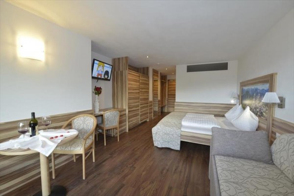 Nowocześnie urządzony pokój hotelowy z łóżkiem, stołem z dwoma krzesłami i telewizorem na ścianie.