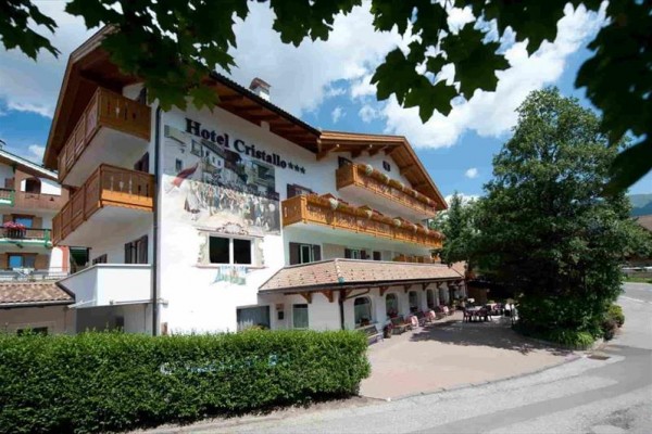 Budynek hotelu Cristallo z balkonem i tarasem, otoczony zielenią.