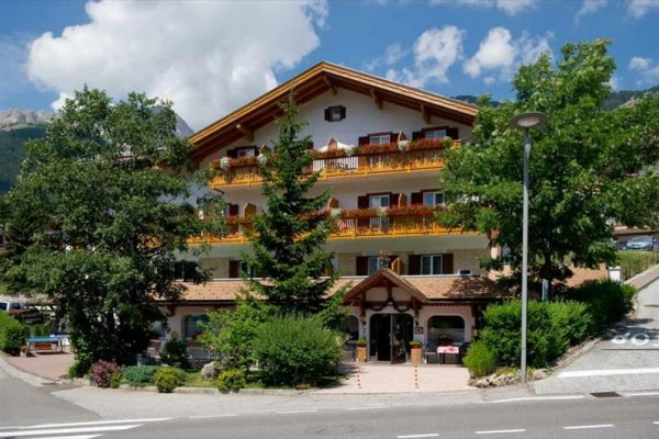 Górski hotel z drewnianymi balkonami otoczony zielenią.