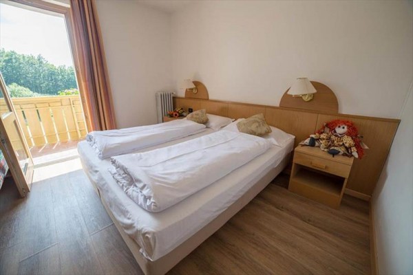 Pokój z podwójnym łóżkiem, stolikiem nocnym i otwartymi drzwiami na balkon.