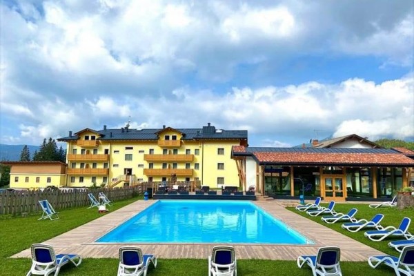 Żółty budynek hotelu z ogrodem i odkrytym basenem otoczonym leżakami.