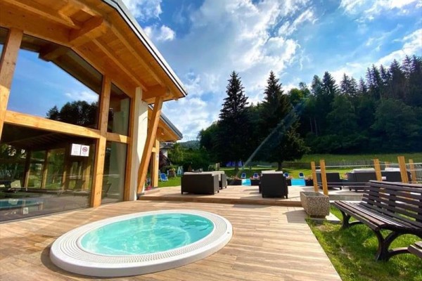 Jacuzzi na tarasie obok nowoczesnego drewnianego domu z widokiem na las.