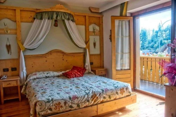 Sypialnia z drewnianym łóżkiem i otwartymi drzwiami na balkon z widokiem na drzewa.