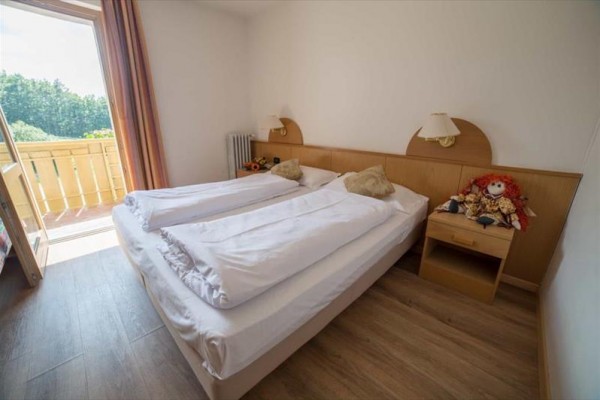 Sypialnia z podwójnym łóżkiem i otwartymi drzwiami na balkon.