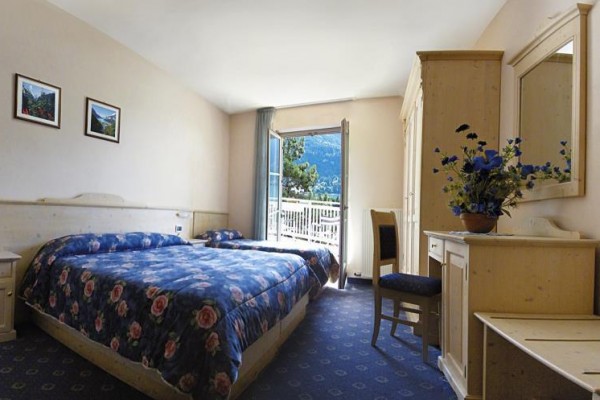 Pokój hotelowy z łóżkiem małżeńskim i otwartym oknem z widokiem na góry.