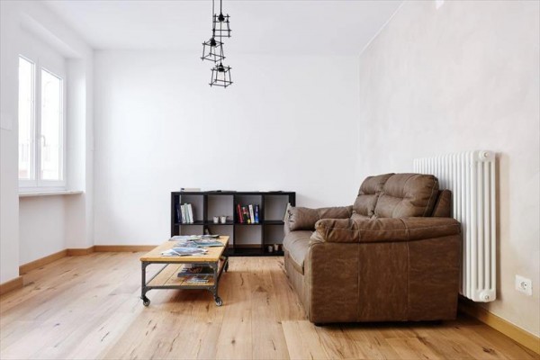 Jasny salon z brązową kanapą, stolikiem kawowym, półką na książki i nowoczesną lampą na suficie.