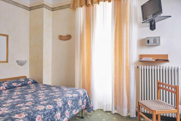 Prosty pokój hotelowy z łóżkiem i telewizorem na ścianie.