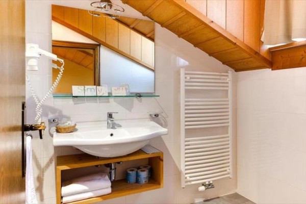 Łazienka ze skośnym sufitem, umywalką, lustrem i grzejnikiem drabinkowym.