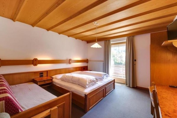 Pokój hotelowy z drewnianym sufitem, łóżkiem małżeńskim, sofą i drzwiami balkonowymi.