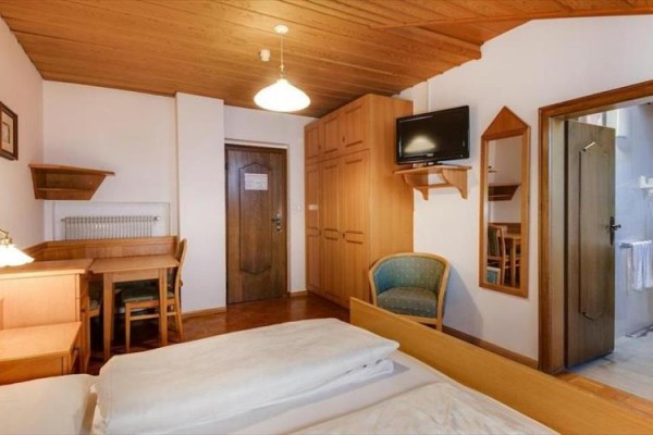 Pokój z drewnianymi meblami, telewizorem, łóżkiem i drzwiami do łazienki.