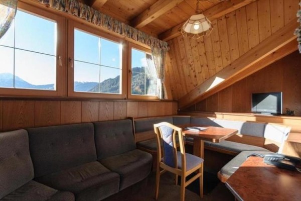 Drewniana poddaszowa przestrzeń mieszkalna z kanapą, stołem jadalnym i telewizorem, z widokiem na góry.