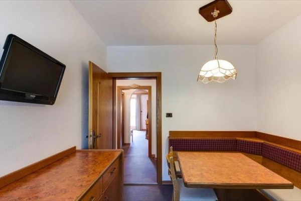 Kącik kuchenny z narożną ławką, stołem i telewizorem na ścianie.