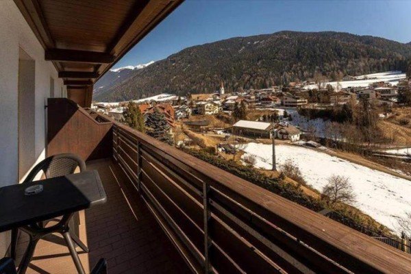 Widok z balkonu na zaśnieżoną wioskę i okoliczne góry.