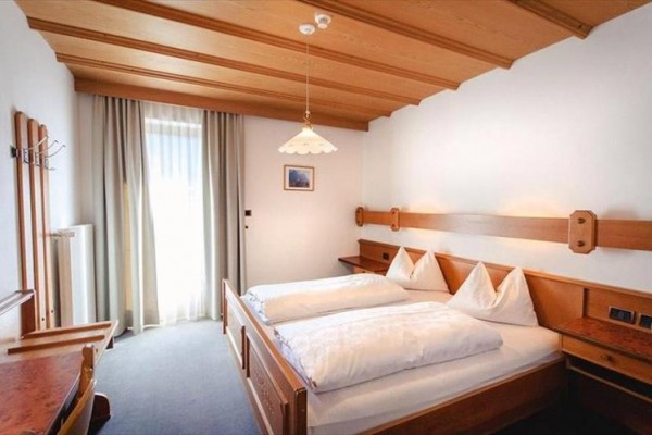 Sypialnia z drewnianymi meblami, łóżkiem małżeńskim i oknem z białymi zasłonami.