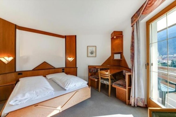 Jasny pokój hotelowy z łóżkiem małżeńskim, biurkiem i dostępem do balkonu.