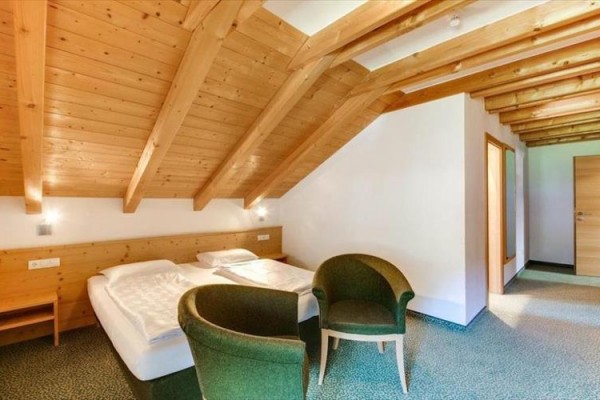 Pokój na poddaszu z łóżkiem małżeńskim i dwoma zielonymi fotelami.