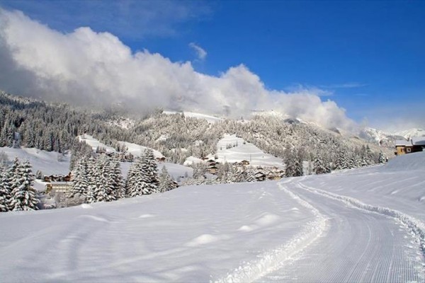 Śniegiem pokryte góry i lasy pod niebieskim niebem z chmurami.