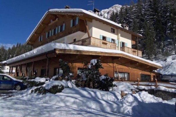 Drewniana górska chata pokryta śniegiem otoczona drzewami.