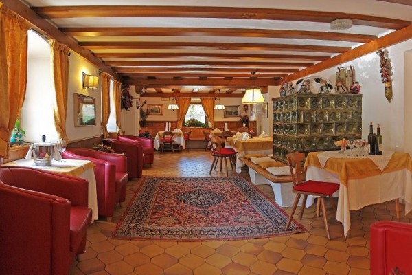 Wnętrze restauracji z drewnianymi sufitami, czerwonymi fotelami i perskim dywanem.
