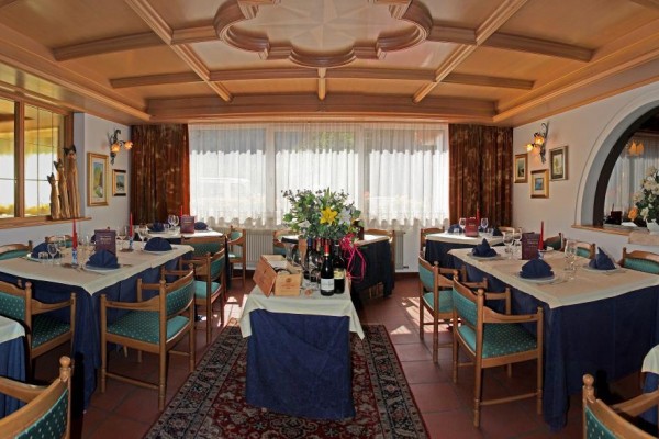 Restauracja z drewnianym sufitem i nakrytymi stołami przy dużych oknach z firankami.