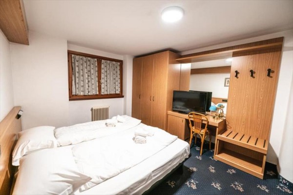 Prosty pokój hotelowy z łóżkiem, szafą, telewizorem i stołem.