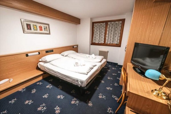 Pokój hotelowy z łóżkiem małżeńskim, telewizorem i drewnianymi meblami.