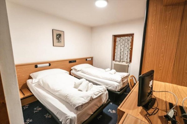 Dwa jednoosobowe łóżka w hotelowym pokoju z drewnianymi meblami i telewizorem.